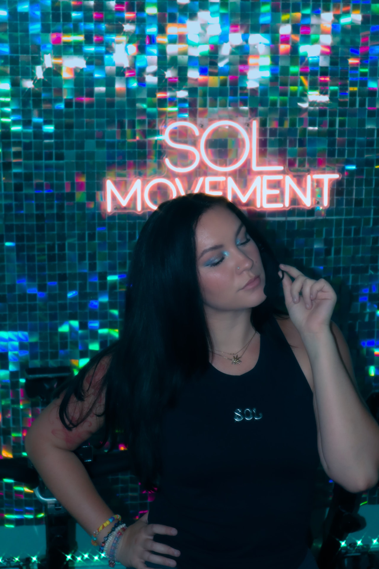 SOL Movement founder standing beneath the lit SOL Movement neon sign in the studio
