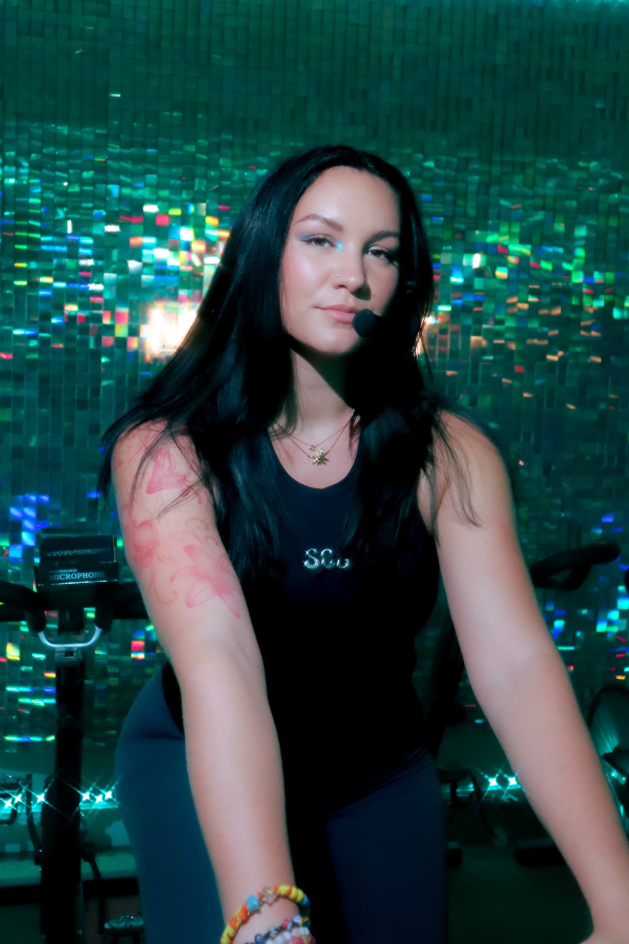 SOL Movement coach on a studio bike wearing a headset mic in front of the sequin wall