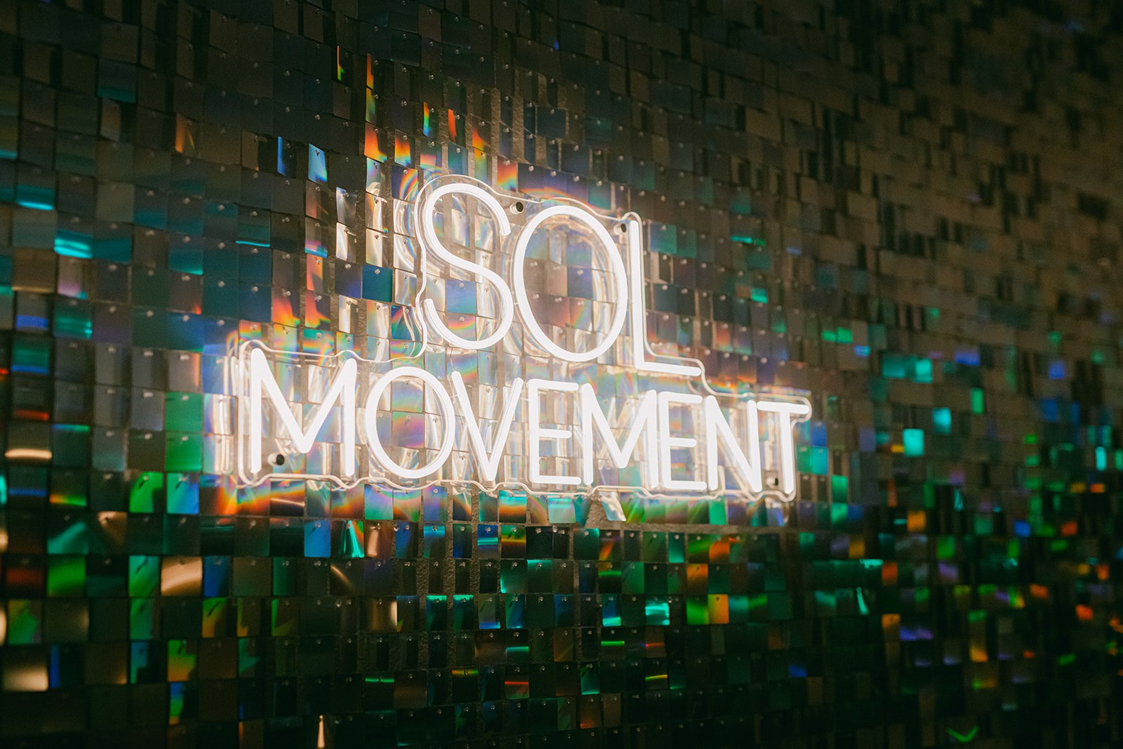 White SOL Movement neon sign glowing on the studio's iridescent sequin wall